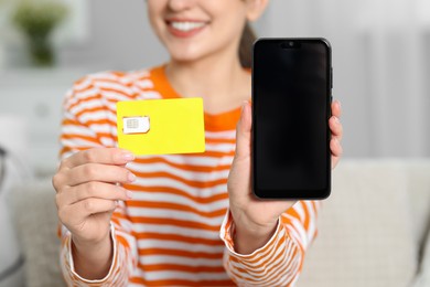 Photo of Woman holding SIM card and smartphone indoors, closeup