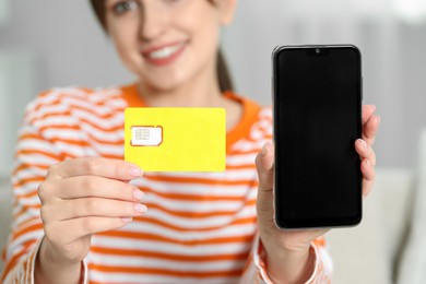Photo of Woman holding SIM card and smartphone indoors, selective focus