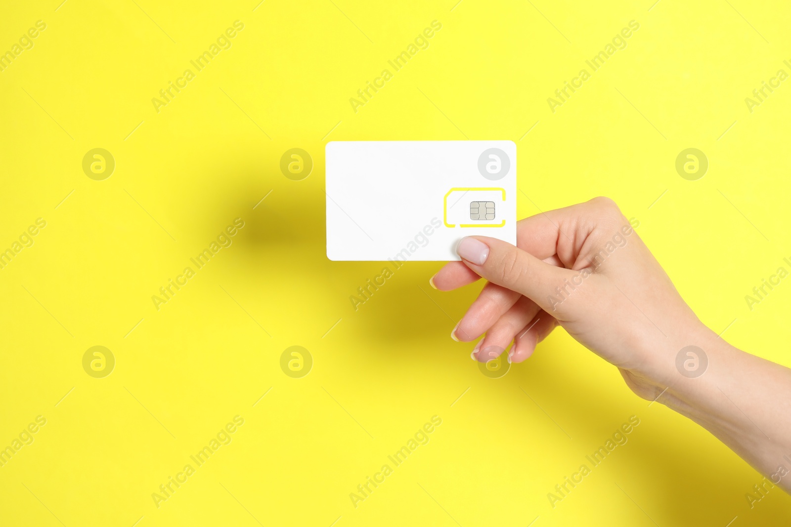 Photo of Woman holding SIM card on yellow background, closeup. Space for text