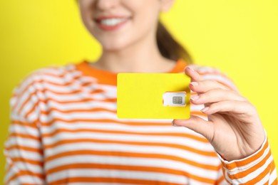 Photo of Woman holding SIM card on yellow background, closeup