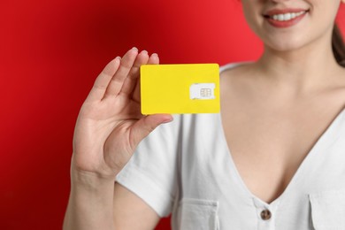 Photo of Woman holding SIM card on red background, closeup