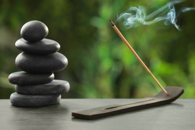 Photo of Incense stick smoldering in holder and spa stones on wooden table outdoors. Om ligature