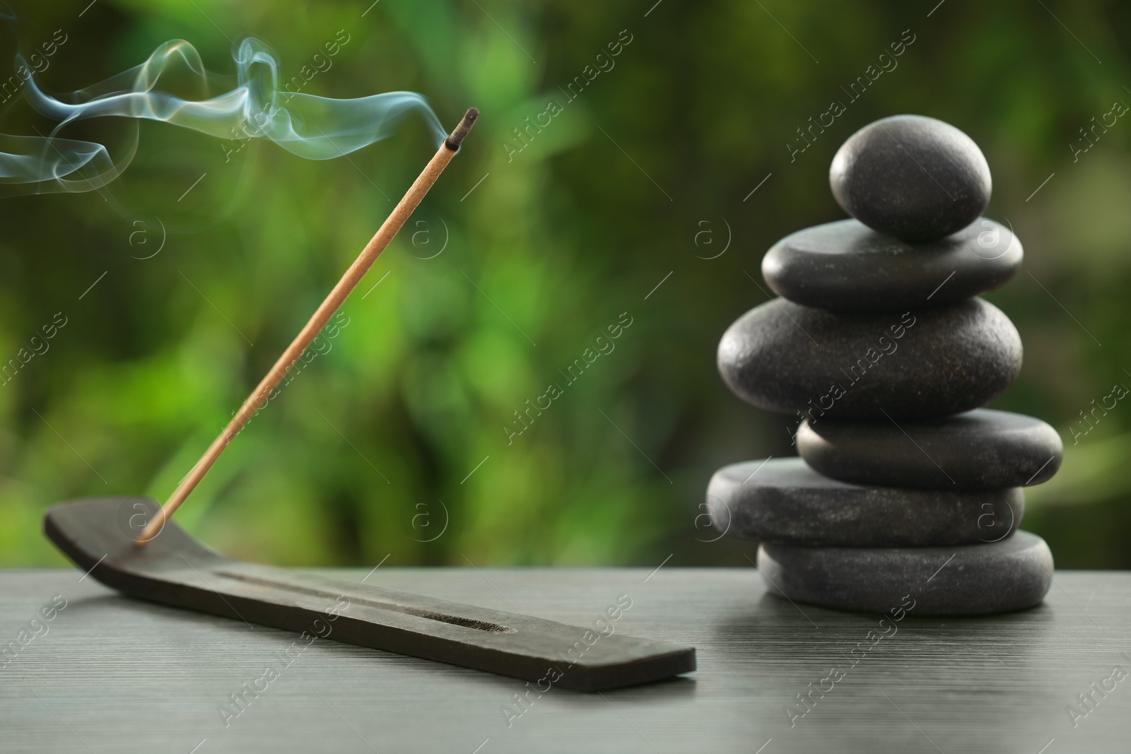 Photo of Incense stick smoldering in holder and spa stones on wooden table outdoors. Om ligature