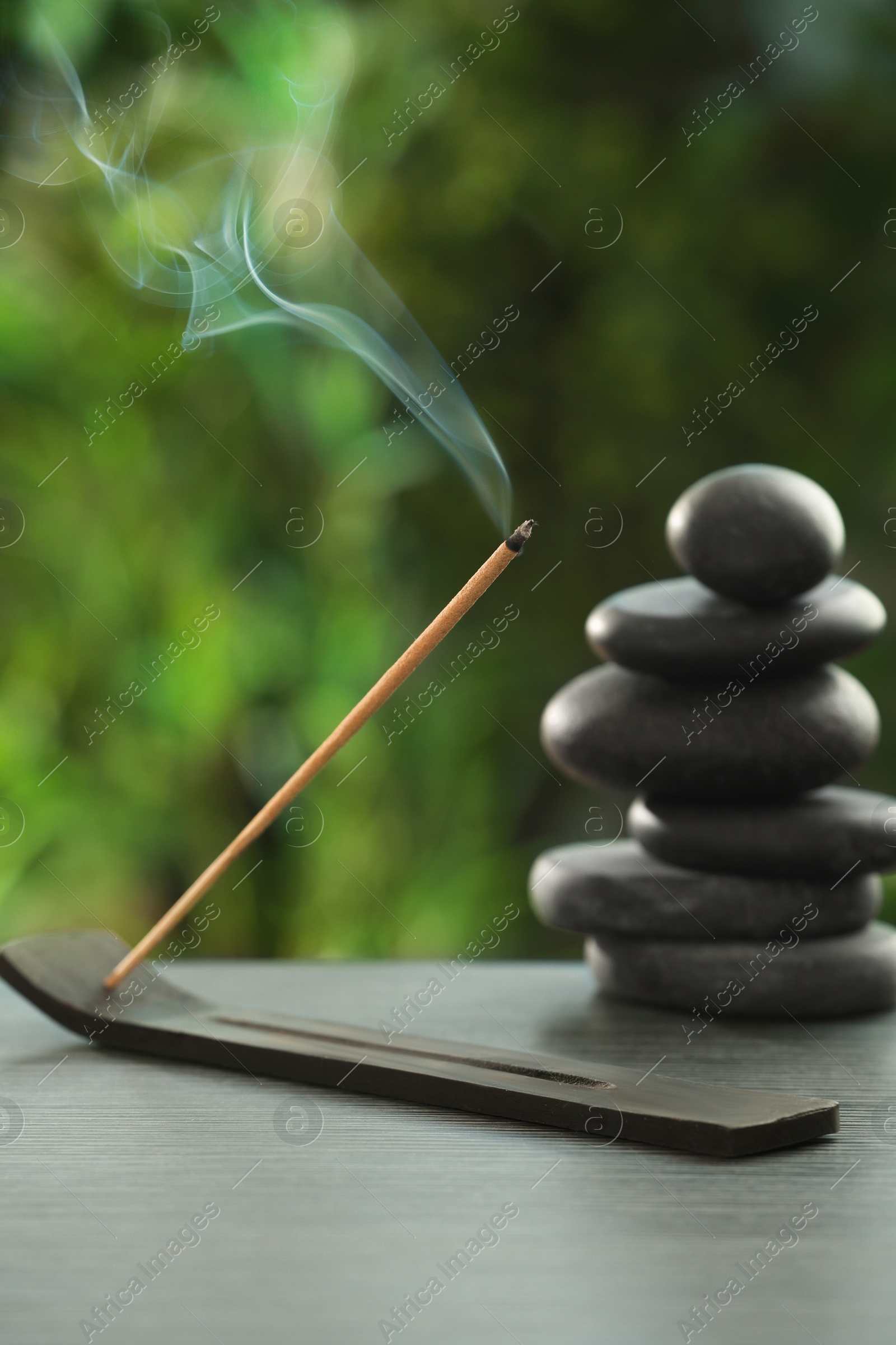 Photo of Incense stick smoldering in holder and spa stones on wooden table outdoors. Om ligature