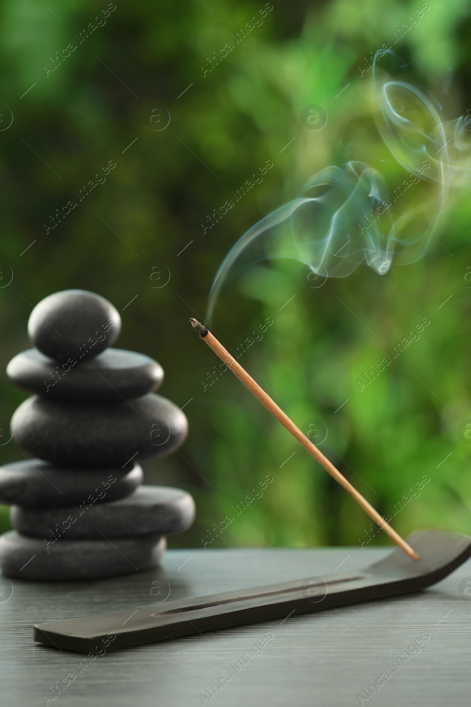 Photo of Incense stick smoldering in holder and spa stones on wooden table outdoors. Om ligature