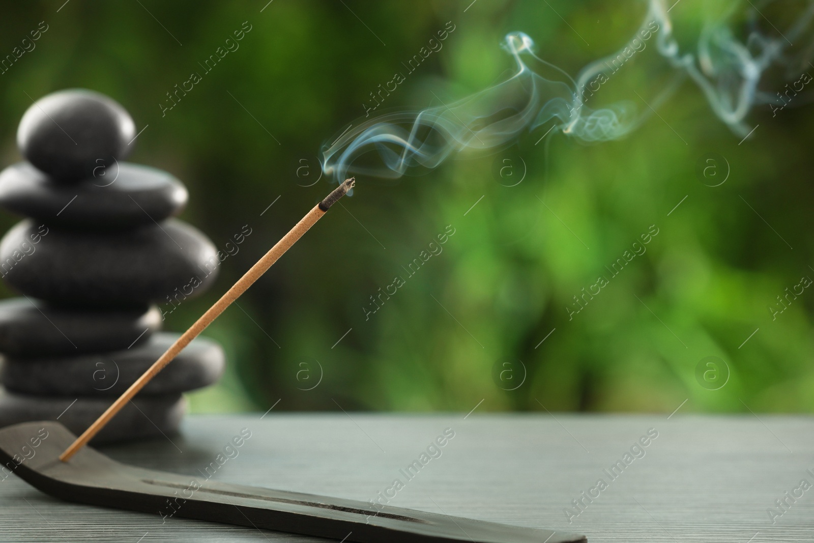 Photo of Incense stick smoldering in holder and spa stones on wooden table outdoors, space for text. Om ligature