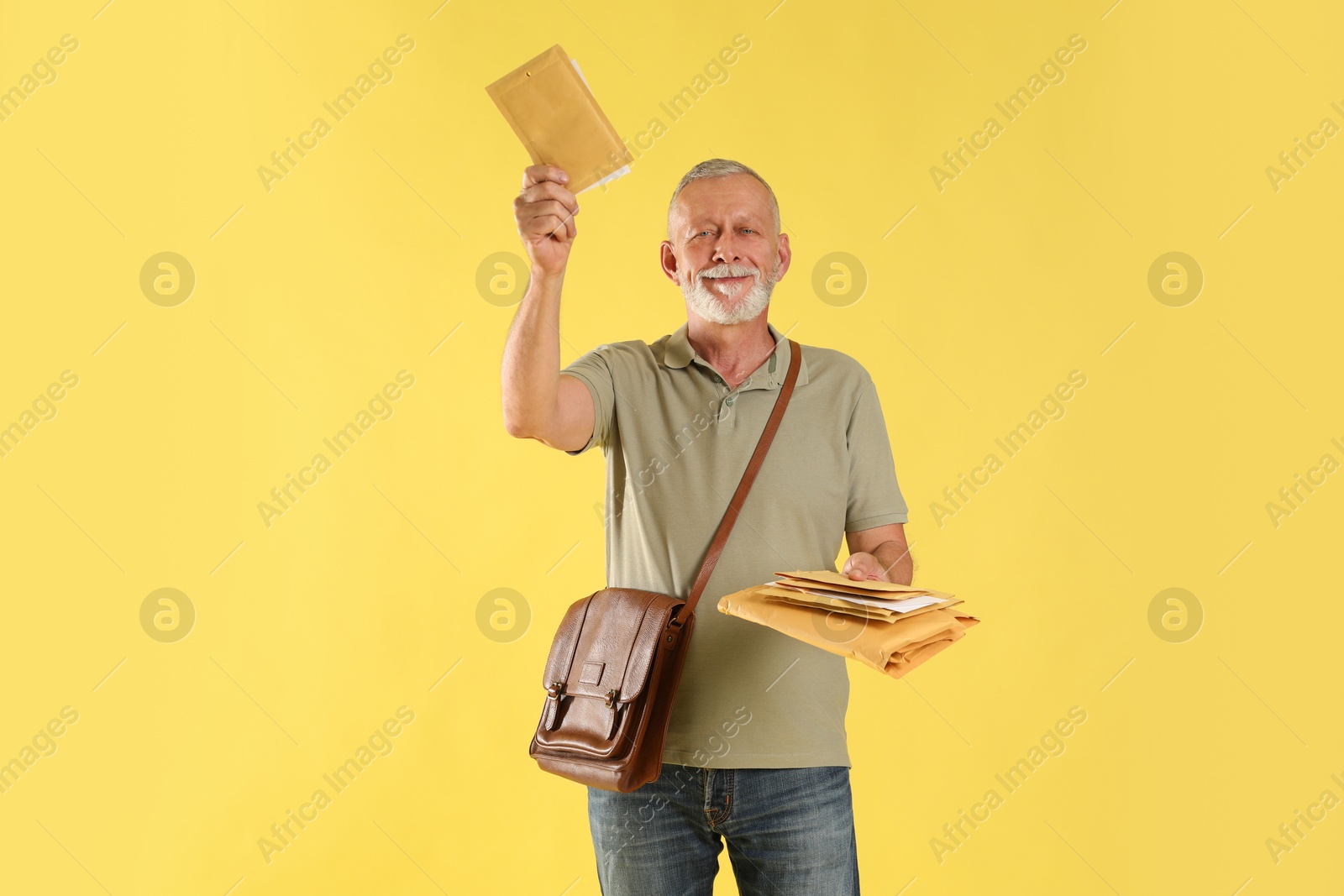 Photo of Happy postman with brown bag delivering letters on yellow background