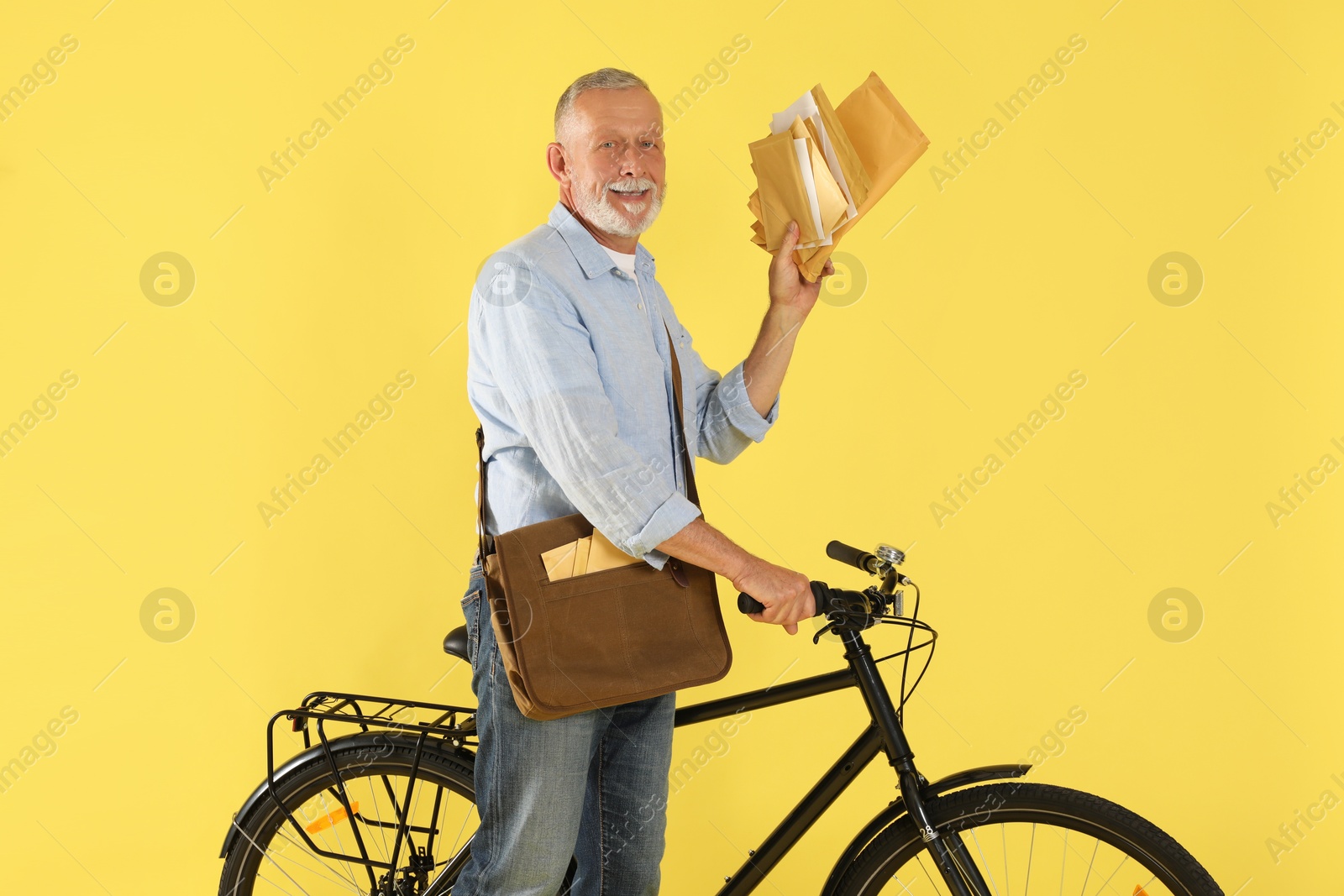 Photo of Happy postman with bicycle delivering letters on yellow background