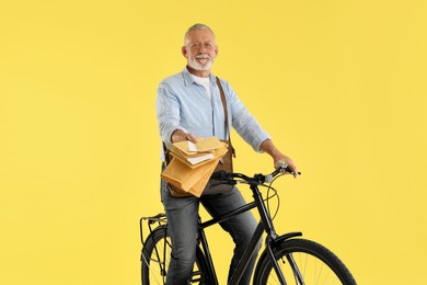 Photo of Happy postman on bicycle delivering letters against yellow background
