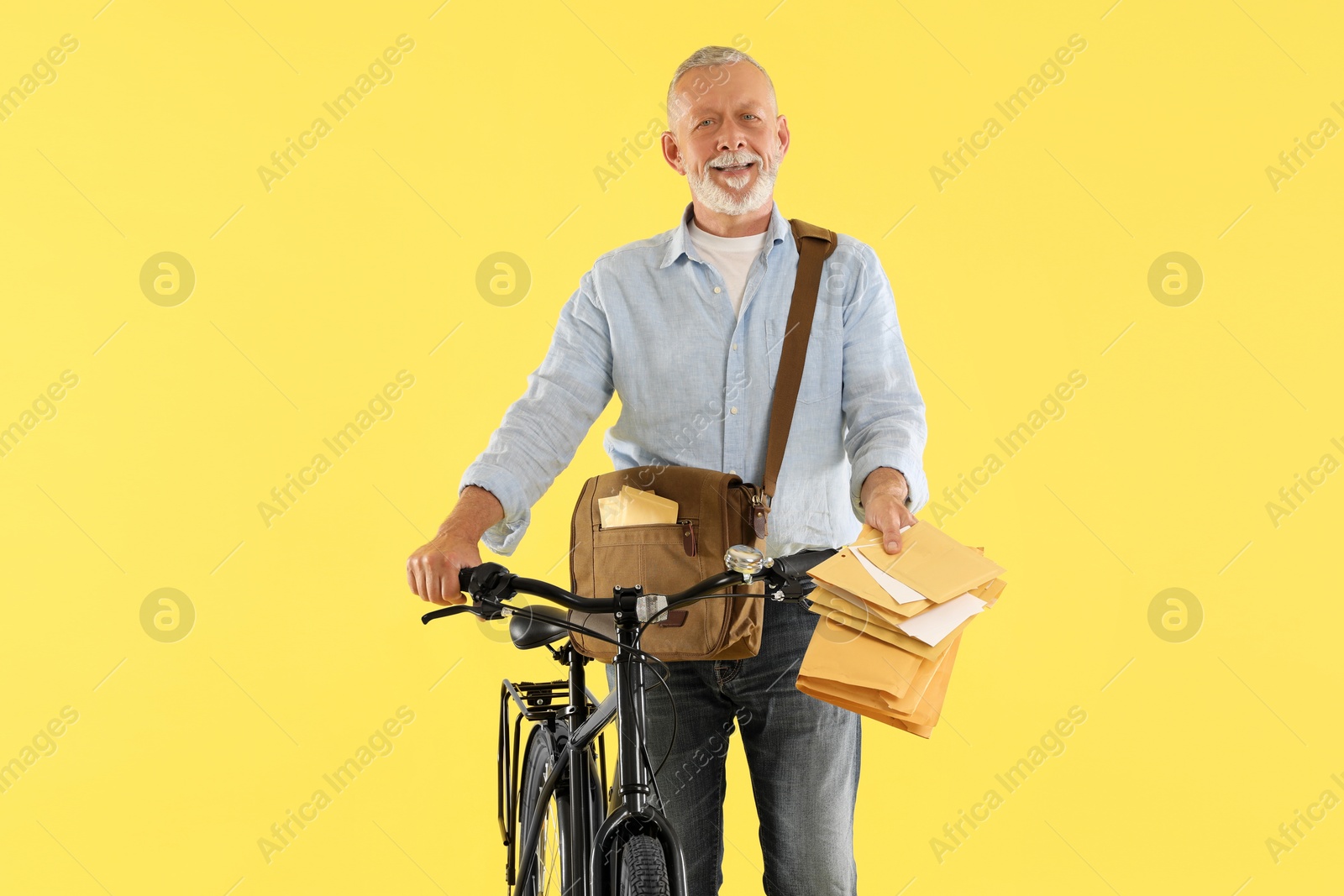 Photo of Happy postman with bicycle delivering letters on yellow background