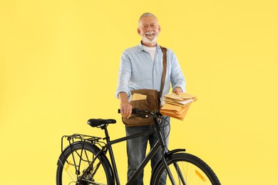 Photo of Happy postman with bicycle delivering letters on yellow background