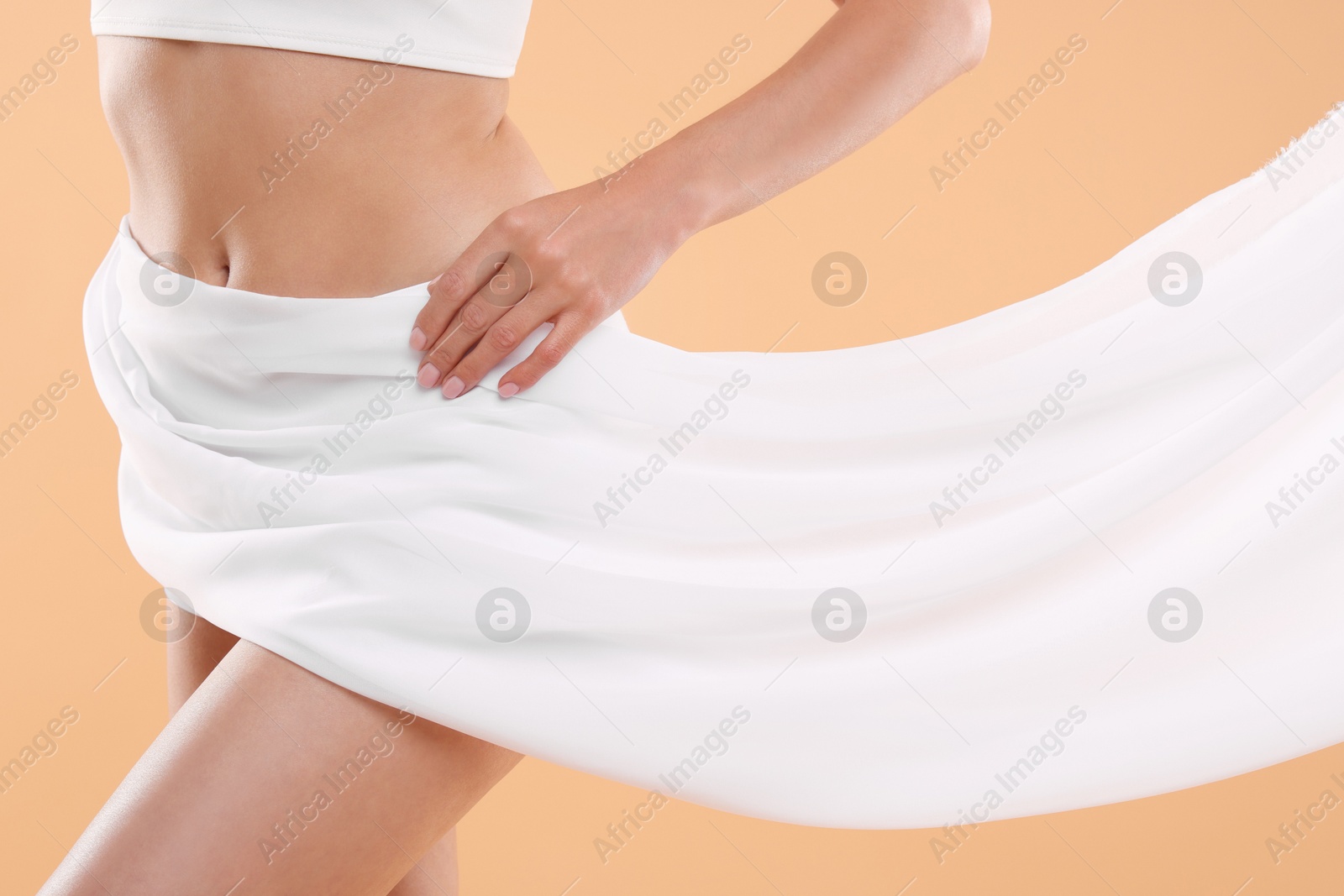 Photo of Diet and weight loss concept. Woman covering her slim body with silk fabric against beige background, closeup