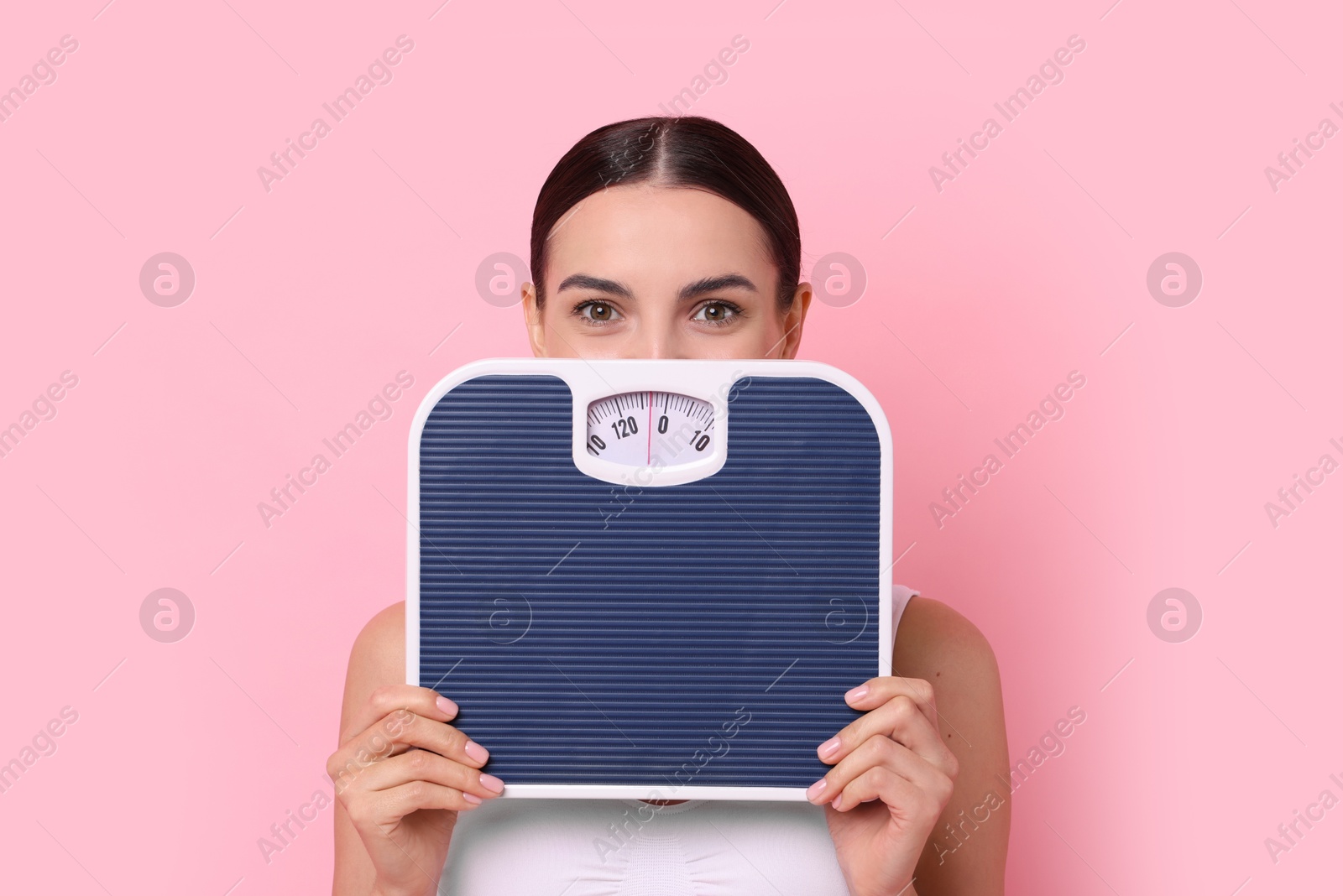 Photo of Diet and weight loss concept. Young woman with floor scale on pink background