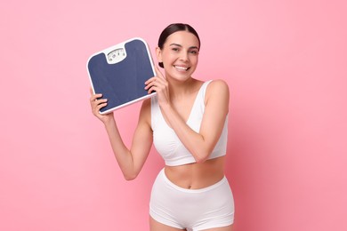 Photo of Diet and weight loss concept. Happy young woman with floor scale on pink background