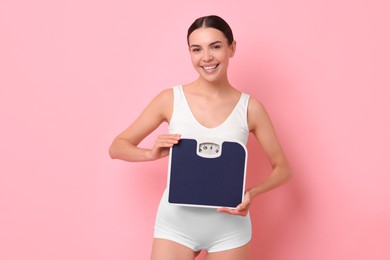 Photo of Diet and weight loss concept. Happy young woman with floor scale on pink background