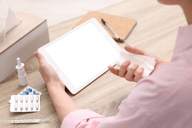 Photo of Sick woman having online consultation with doctor via tablet at wooden table, closeup