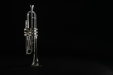 Shiny trumpet on black background, space for text. Wind musical instrument