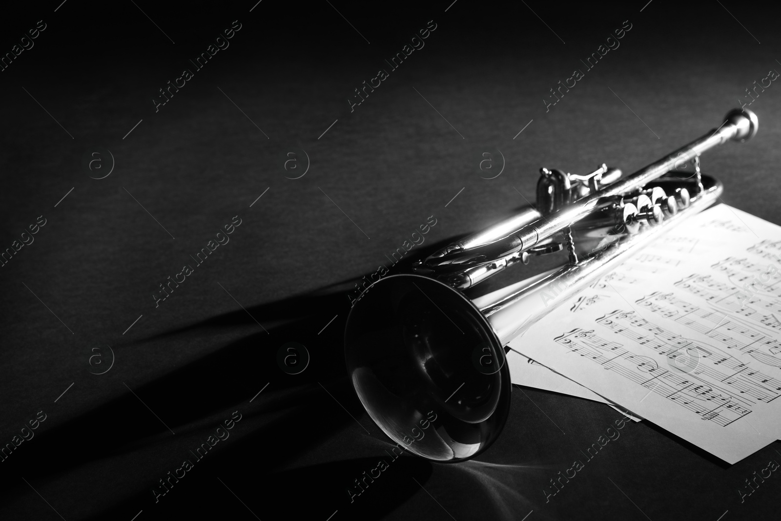 Photo of Shiny trumpet and music sheets on dark background, space for text. Wind musical instrument