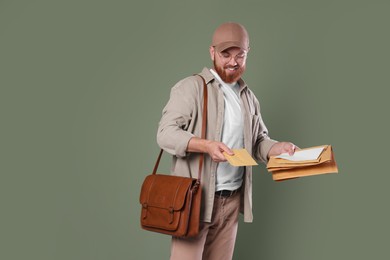 Photo of Happy young postman with brown bag delivering letters on olive background