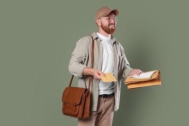 Photo of Happy young postman with brown bag delivering letters on olive background