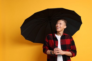 Photo of Young man with black umbrella on yellow background