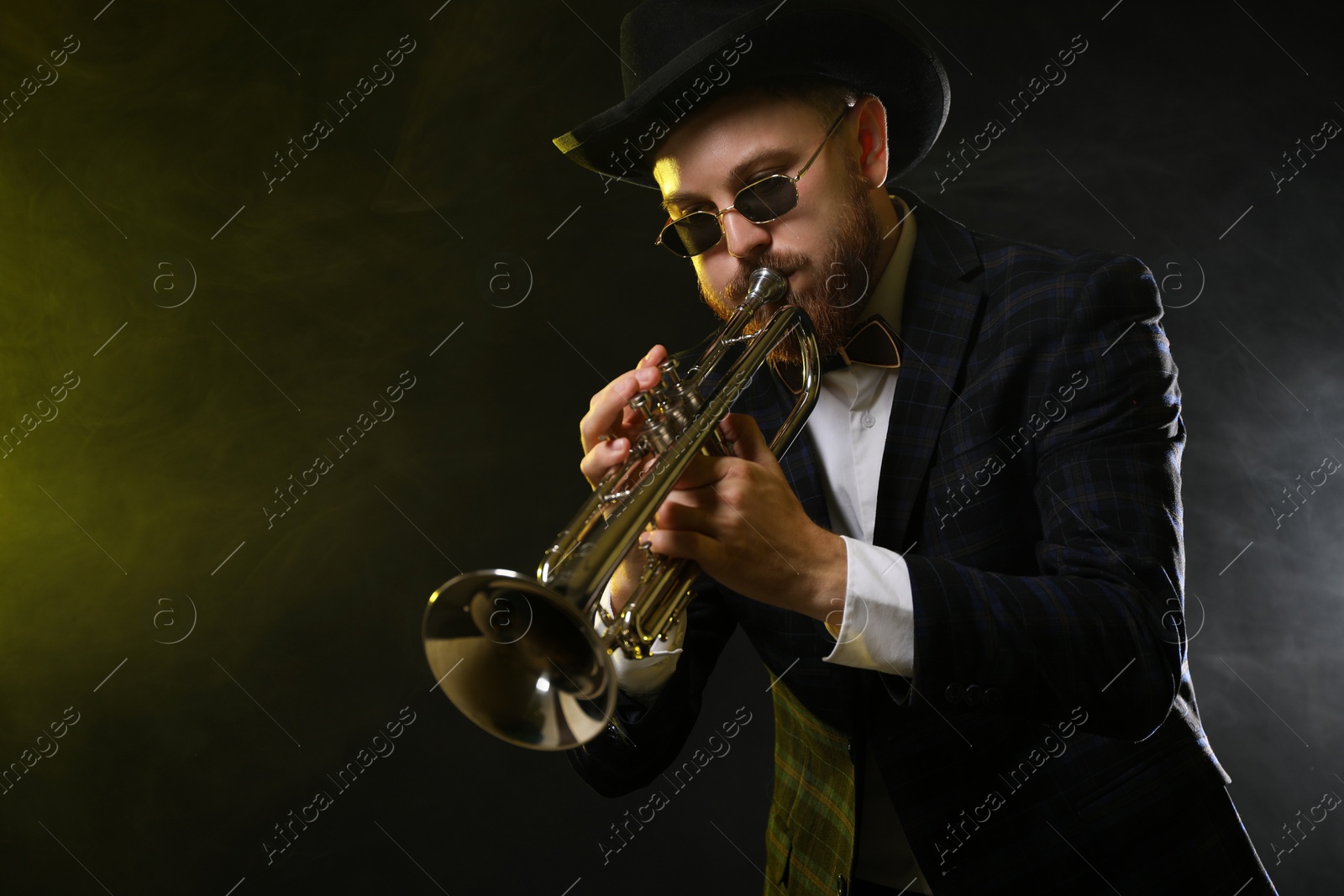 Photo of Professional musician playing trumpet on black background in color lights and smoke. Space for text