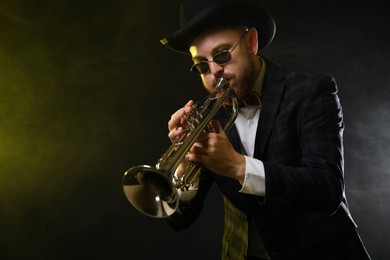 Photo of Professional musician playing trumpet on black background in color lights and smoke. Space for text