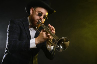 Photo of Professional musician playing trumpet on black background in color lights and smoke. Space for text