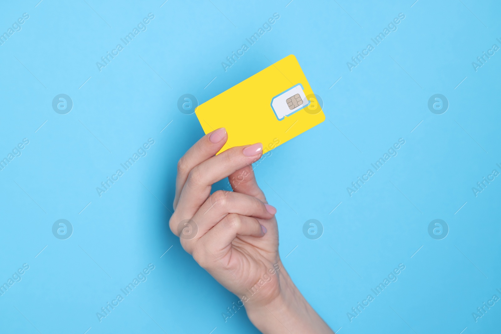 Photo of Woman holding SIM card on light blue background, closeup