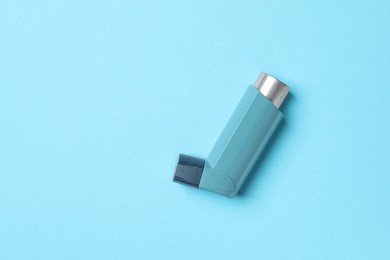 Photo of Asthma inhaler on light blue background, top view. Space for text