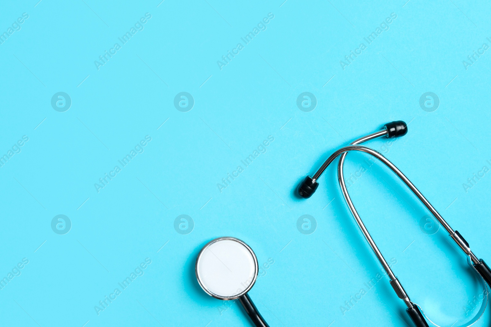 Photo of Stethoscope on light blue background, top view. Space for text