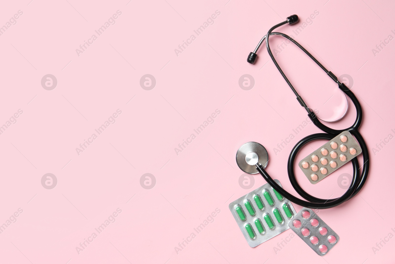 Photo of Stethoscope and pills on pink background, flat lay. Space for text