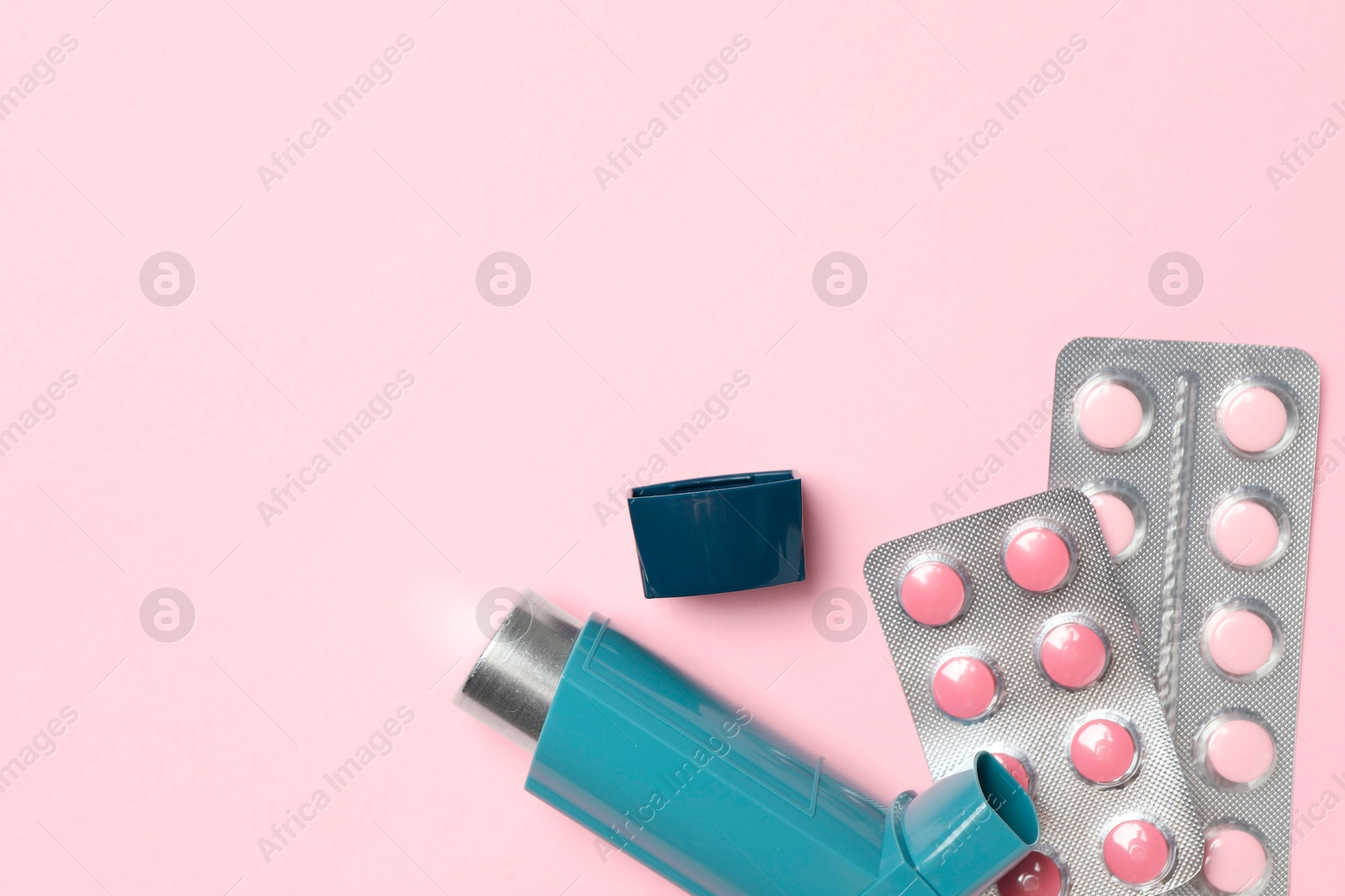 Photo of Asthma inhaler and pills on pink background, flat lay. Space for text