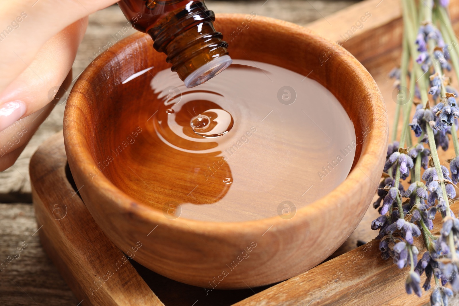 Photo of Woman dripping essential oil into bowl with water at wooden table, closeup