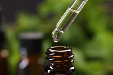 Dripping essential oil into bottle on blurred background, closeup