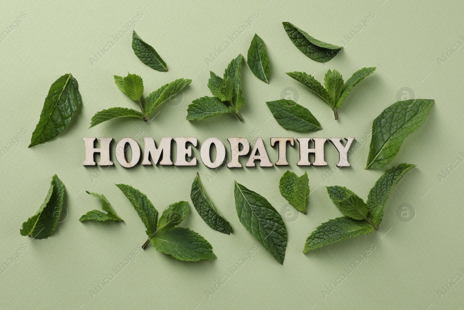 Photo of Word Homeopathy and mint leaves on olive background, flat lay