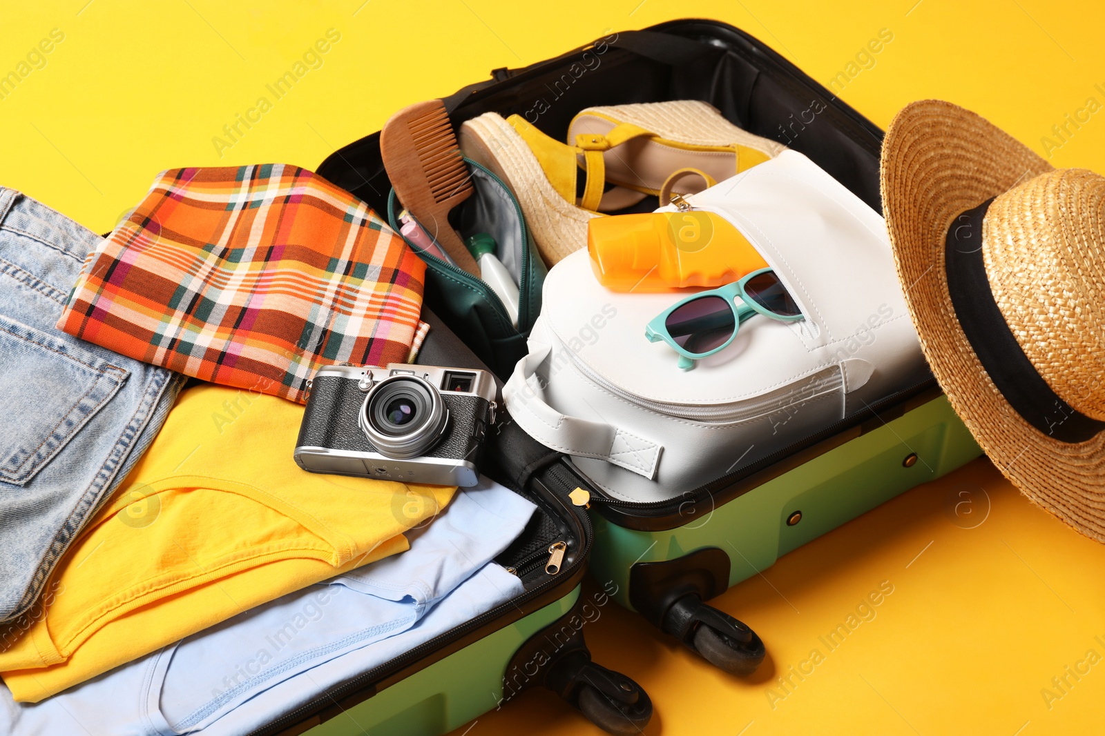 Photo of Open suitcase with traveler's belongings on yellow background, closeup