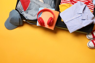 Photo of Open suitcase with traveler's belongings on yellow background, flat lay. Space for text