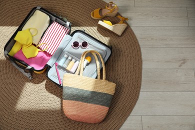 Open suitcase with traveler's belongings on rug, flat lay. Space for text