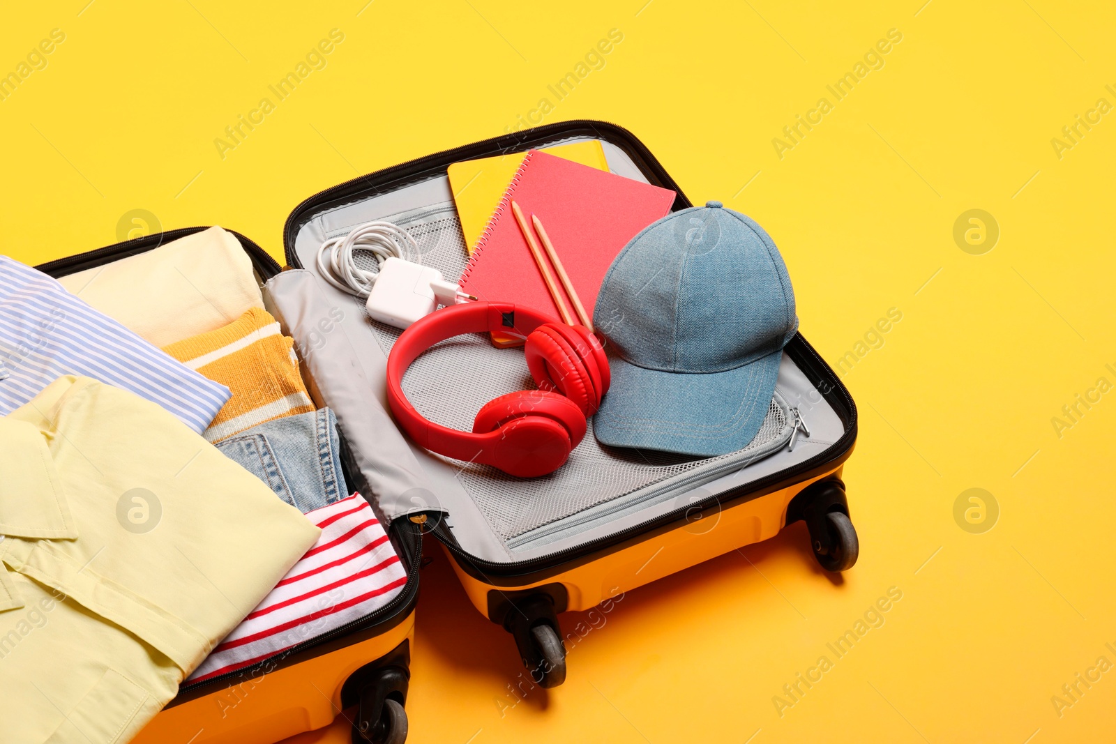 Photo of Open suitcase with traveler's belongings on yellow background