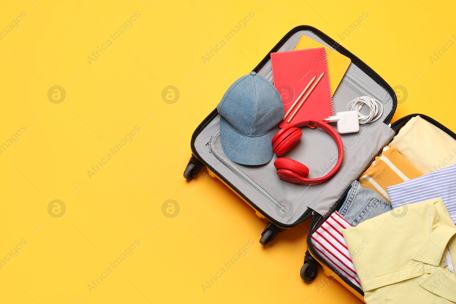 Photo of Open suitcase with traveler's belongings on yellow background, top view. Space for text