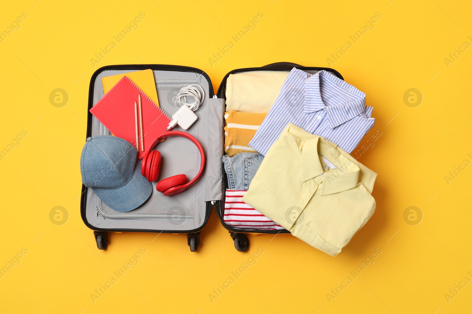 Photo of Open suitcase with traveler's belongings on yellow background, top view