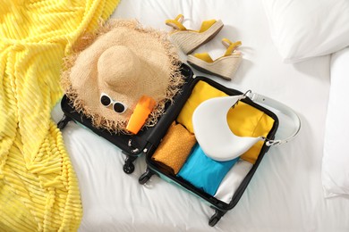 Open suitcase with traveler's belongings on bed, flat lay