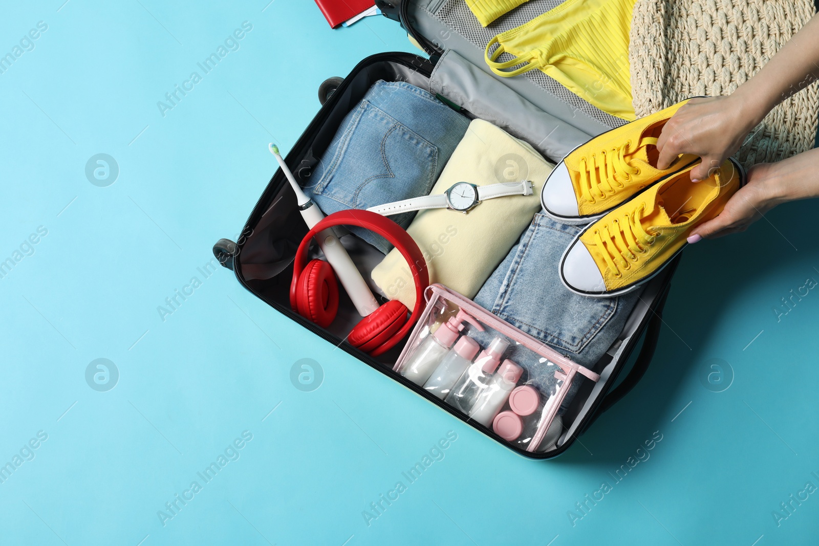 Photo of Woman packing suitcase on light blue background, top view. Space for text