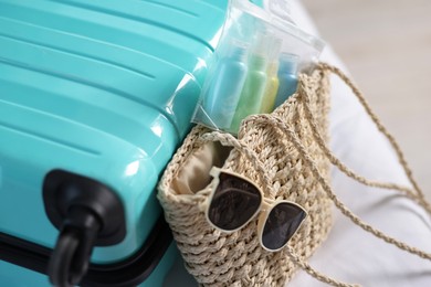 Photo of Turquoise suitcase, bag, sunglasses and cosmetic travel kit on bed indoors, closeup