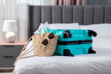 Turquoise suitcase, bag, sunglasses and cosmetic travel kit on bed indoors