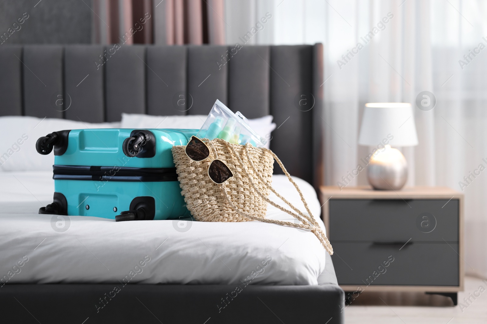 Photo of Turquoise suitcase, bag, sunglasses and cosmetic travel kit on bed indoors