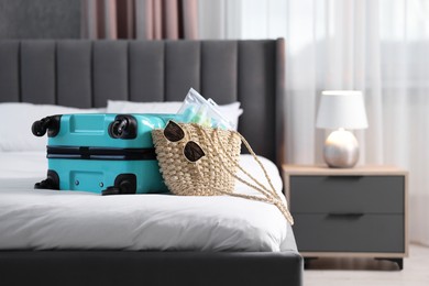 Turquoise suitcase, bag, sunglasses and cosmetic travel kit on bed indoors