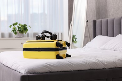 Photo of Yellow suitcase, headphones and vintage camera on bed indoors