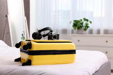 Photo of Yellow suitcase, headphones and vintage camera on bed indoors